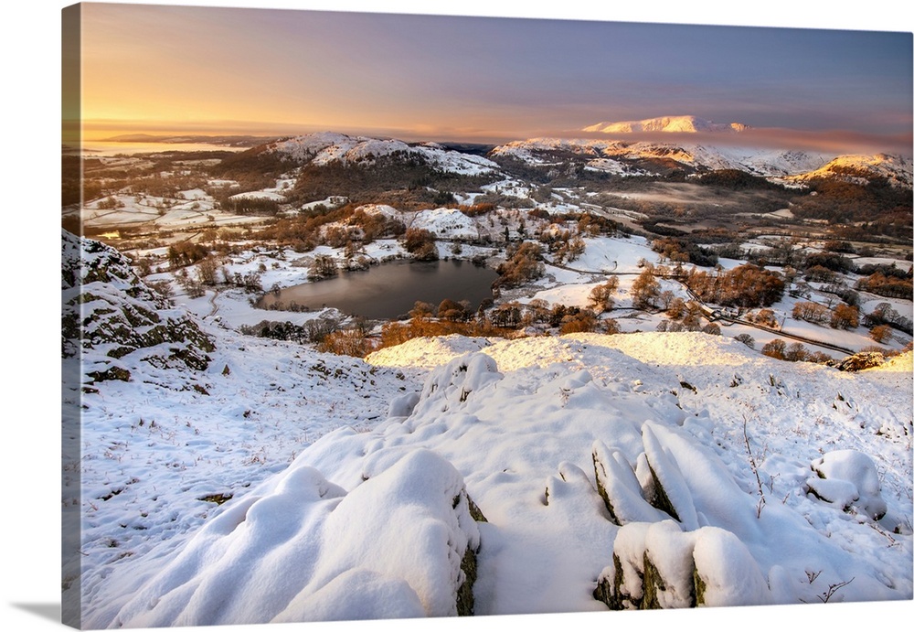 View from Loughrigg Fell on a winter morning with golden light bathing the snow covered landscape in Lake District, UK.