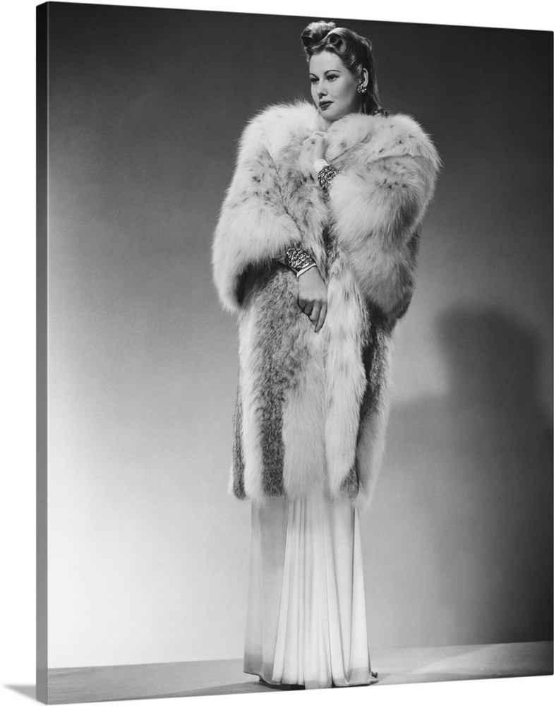 Sophisticated woman in evening gown and fur coat posing in studio, (B&W), portrait