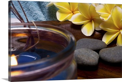 Spa elements: candle, plumeria flowers, and grey stones