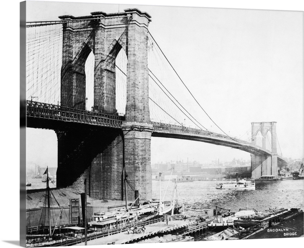 View of the Brooklyn Bridge showing docks and boat passing underneath.