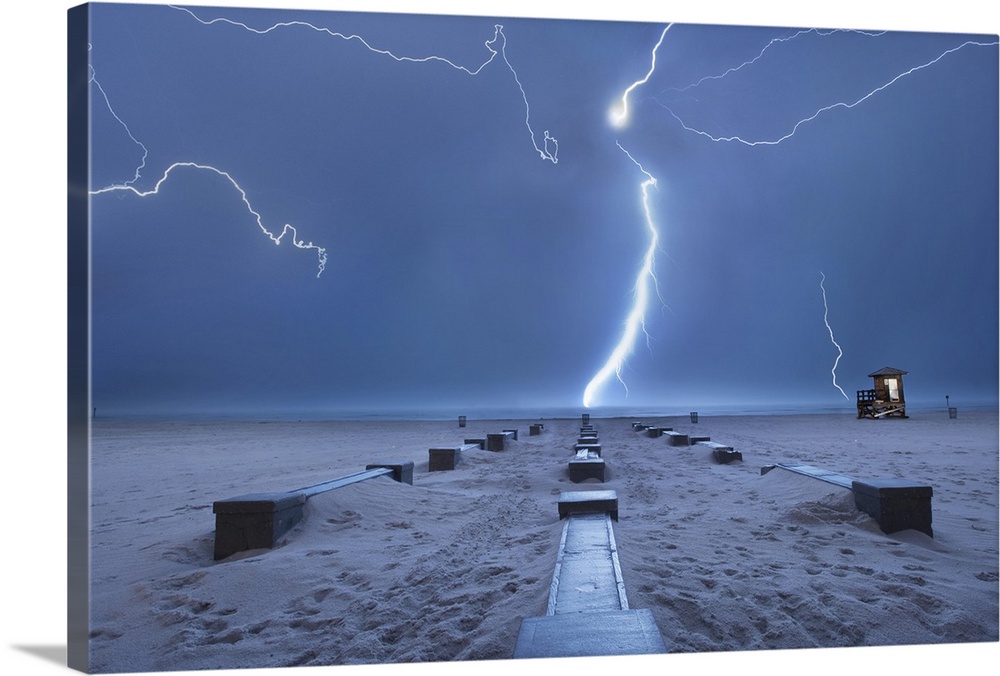 Bolts of lightening light up a dreary sky as rows of benches sit on the sandy beach.