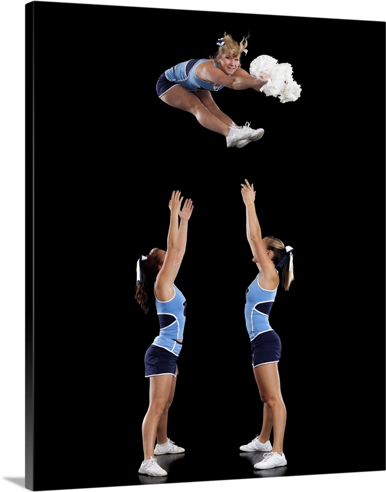 Studio shot of cheerleaders (16-17) assisting friend during jump