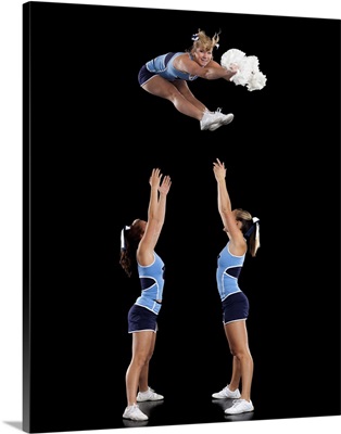 Studio shot of cheerleaders assisting friend during jump