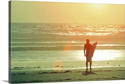 Surfer stands by shore as sun goes down.