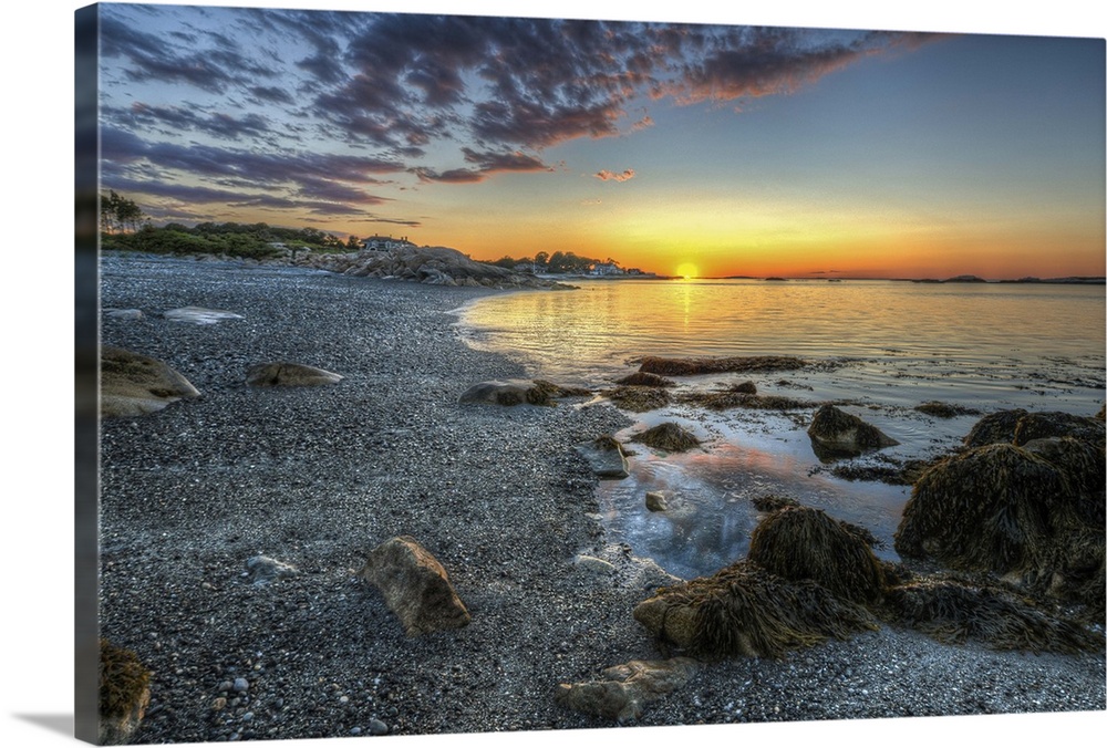 A colorful sunset on a beach with rocks and stones in the foreground.