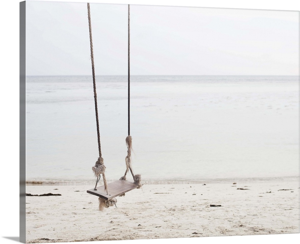 Swing made out of ropes and wood over a sandy beach directly on the ocean. The swing looks like an invite for everyone to ...