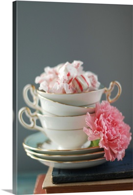 Teacups stacked on books with candy and pink carnation.