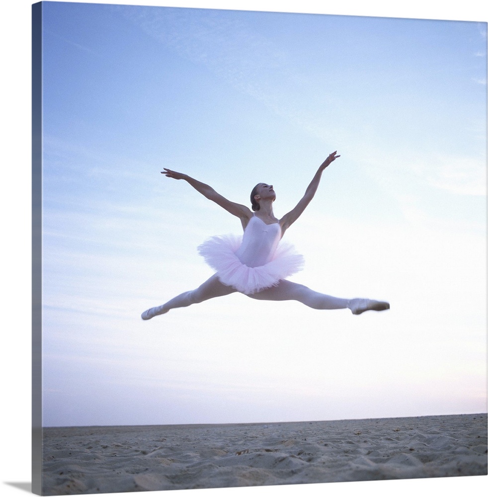 Teenage ballerina (16-18) performing leap on beach, low angle view
