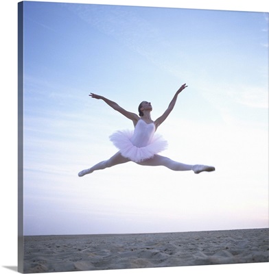 Teenage ballerina performing leap on beach, low angle view