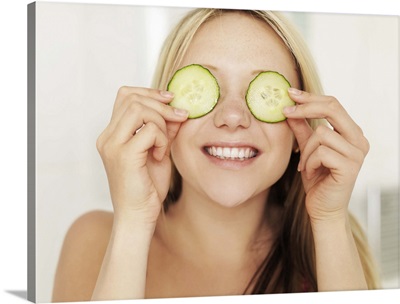 Teenage girl covering eyes with cucumber slices