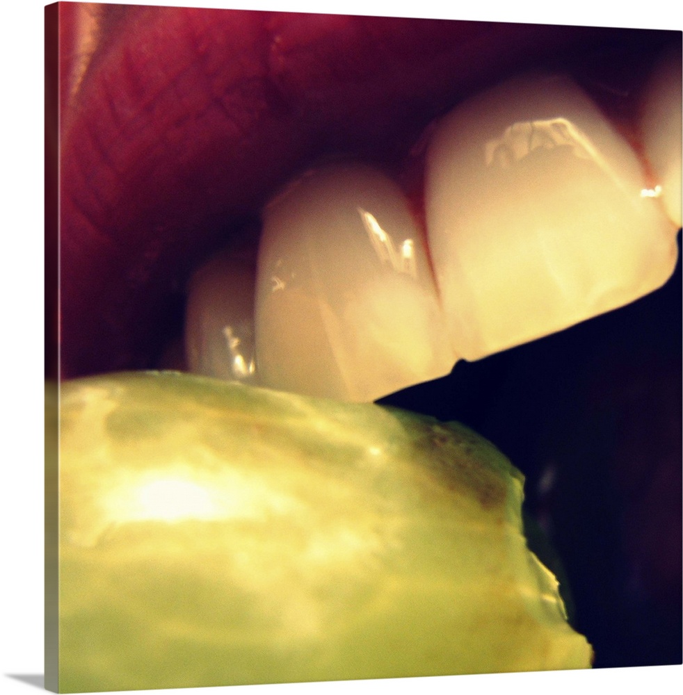 Partial mouth and teeth biting green grape.