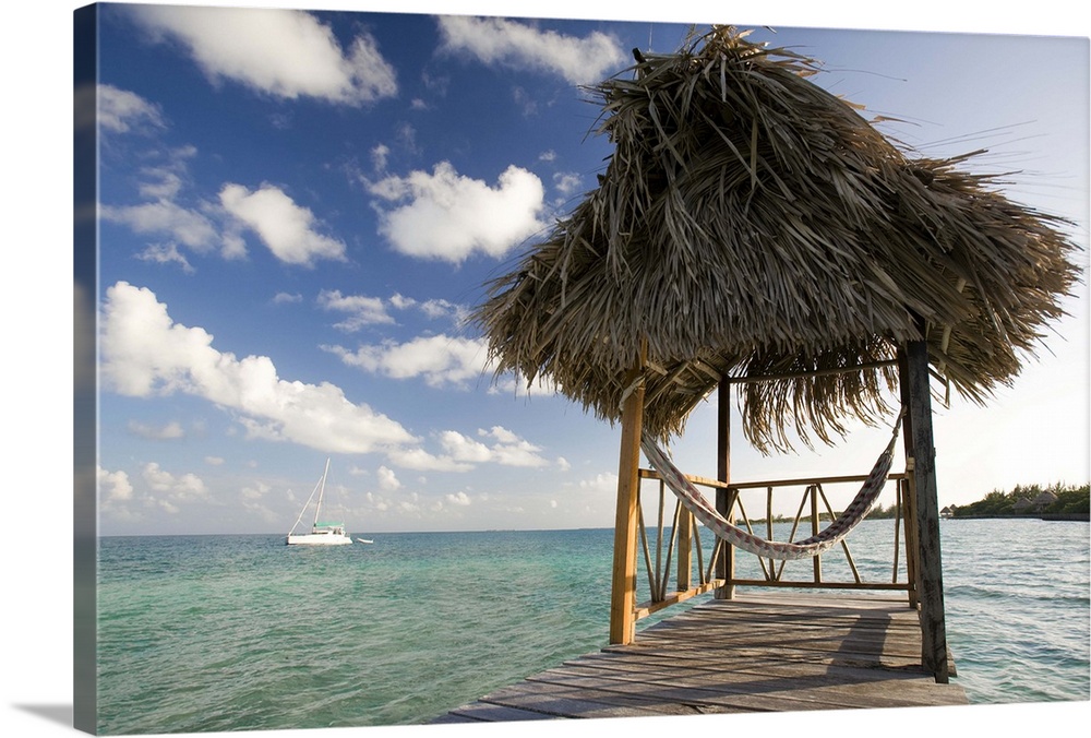 Thatch hut and hammock on dock over the Caribbean in Belize on Thatch Caye. Sailboat in the background, shot midday.