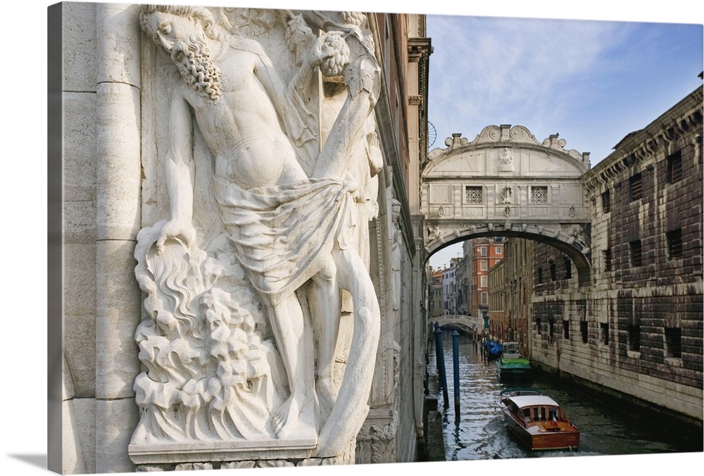 Large photograph taken of a bridge in Italy with a boat floating under it and a statue of a man in the forefront of the pi...