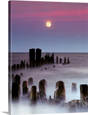 The full moon rises over Lake Michigan as rolling waves wash over the remnant of a pier.