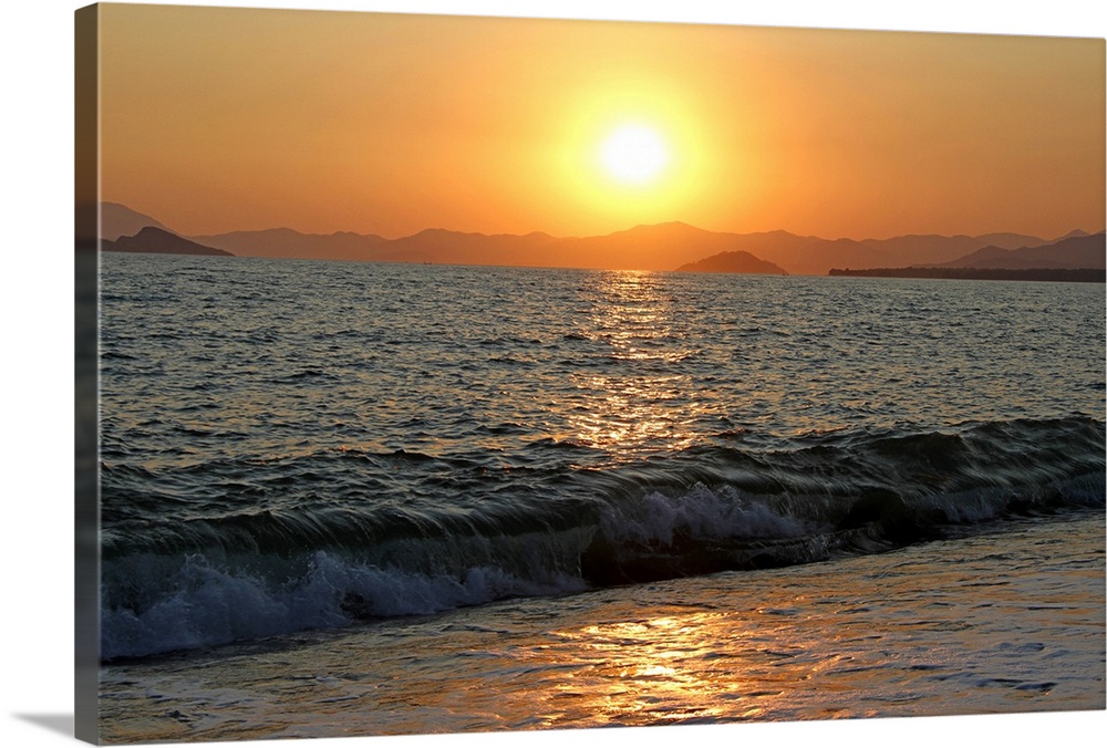 The sun sets over a beautiful mountain range, whilst the sea laps away in the foreground.