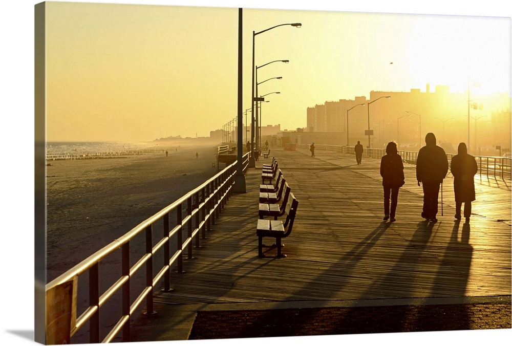 Three people walking down boardwalk near beach at sunset. Wall Art