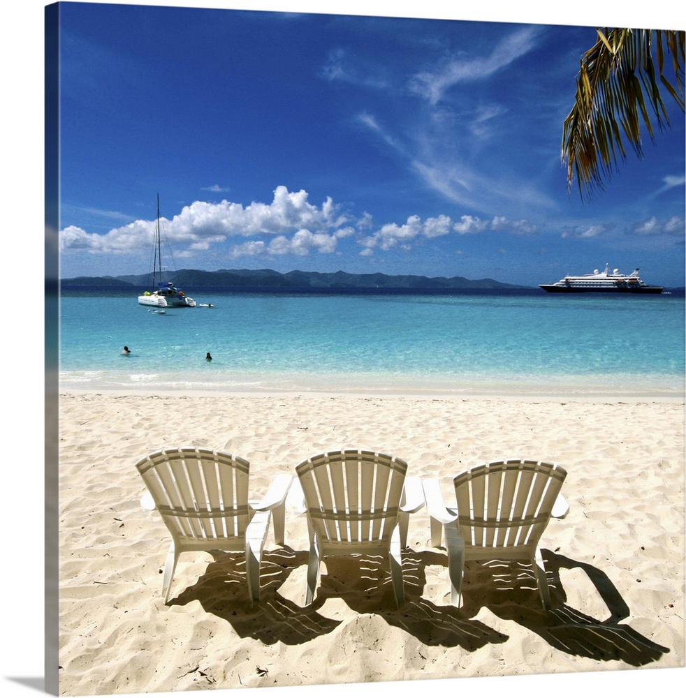 Idyllic white sandy beach with three white plastic scalloped chairs on the beach overlooking an cyan aquarmarine blue sea ...