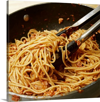 Tongs tossing spaghetti with meat sauce in pan