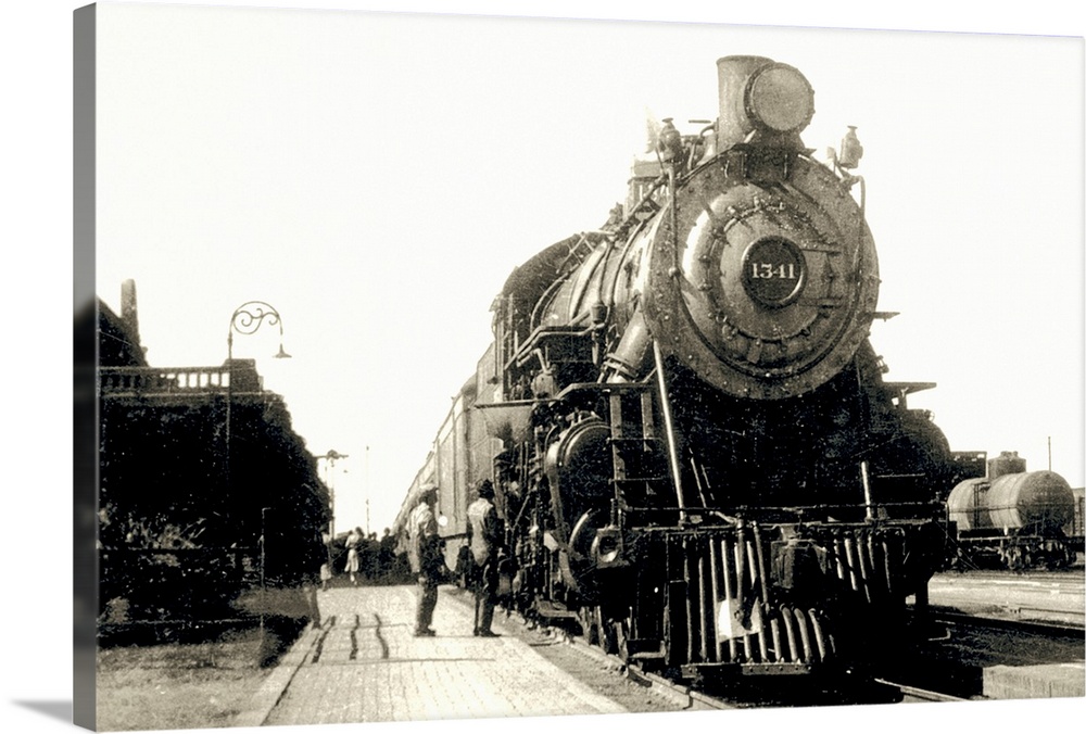 This is a vintage photograph of a locomotive being admired by two men at a train station.