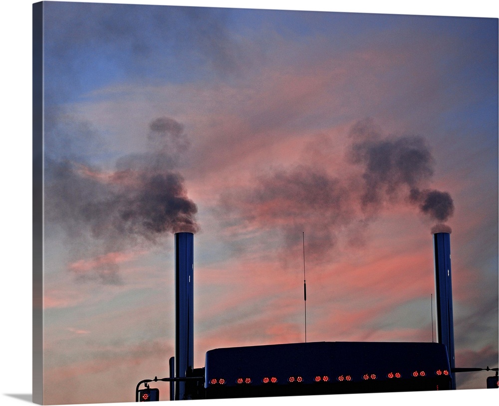 Semi-truck emitting black smoke from dual exhaust pipes against sunset, low angle view.