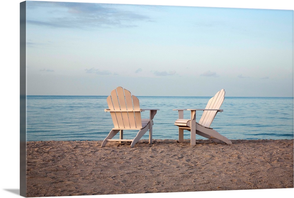 Two adirondack chairs on the beach.