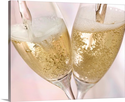 Two champagne flutes being filled with sparkling champagne in celebration