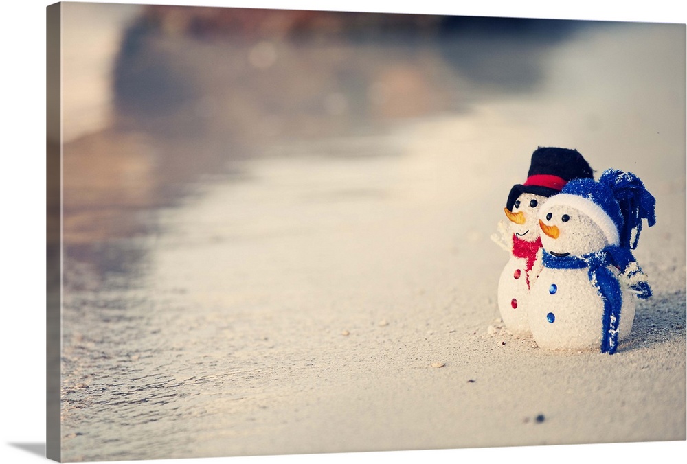 Christmas time in warm weather. Waves on the white sand. Two snowman looking out to sea. Christmas decorations. Red and bl...