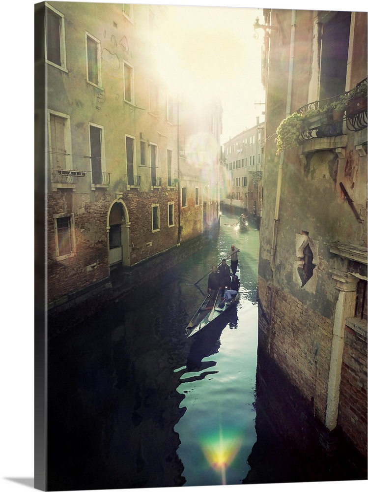 Portrait, oversized photograph of two gondolas floating toward the bright sun, through a canal in Italy, with tall buildin...