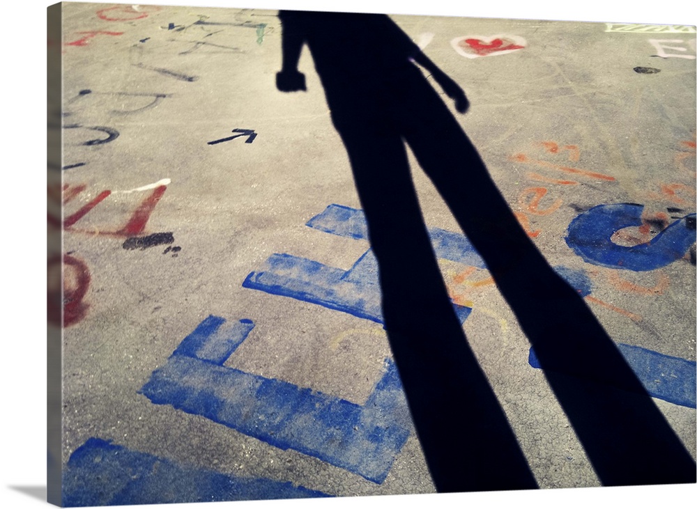 Man taking snapshot of his shadow together with colorful graffiti and tag lines on ground.