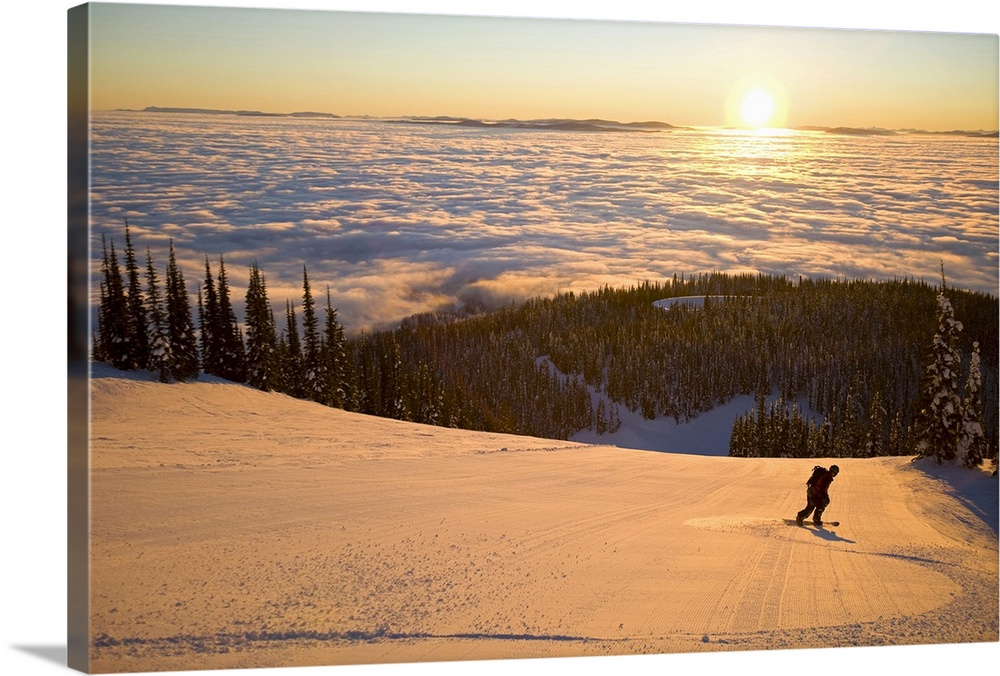 Oversized horizontal photograph of a man snowboarding down a hill that is high above a winter landscape below, where a lar...