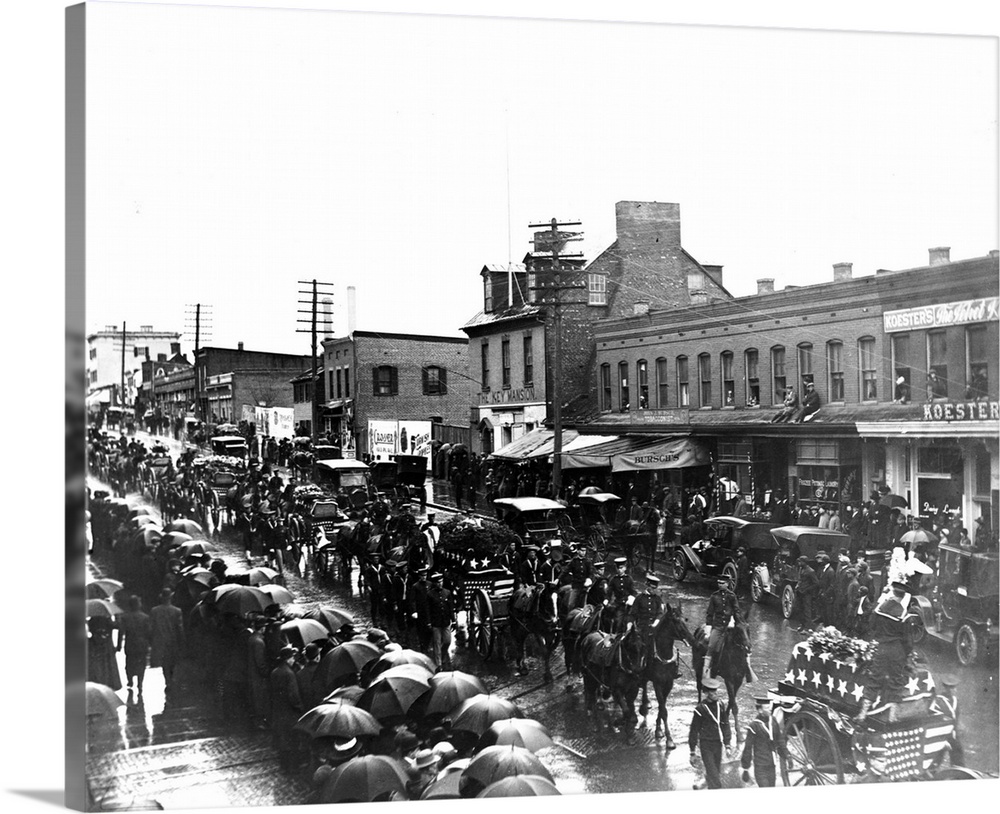 Under the cover of umbrellas, people line the sidewalks of M Street in Georgetown to view the funeral procession for USS M...