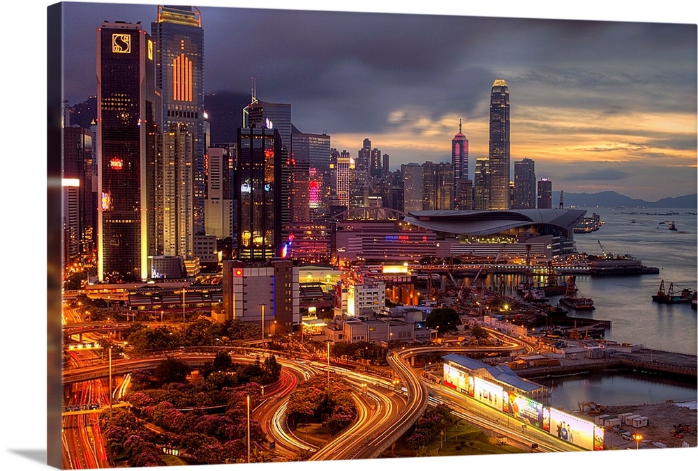 Big landscape photograph of winding roads lading around and through the city of Hong Kong.  Skyscrapers are brightly lit b...