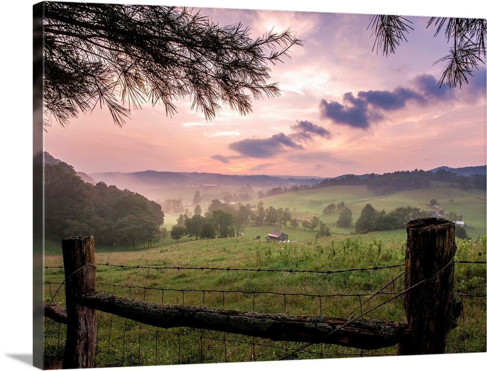 Old fence with barbwire and pine tree help frame picturesque image of the country farmland in evening light.