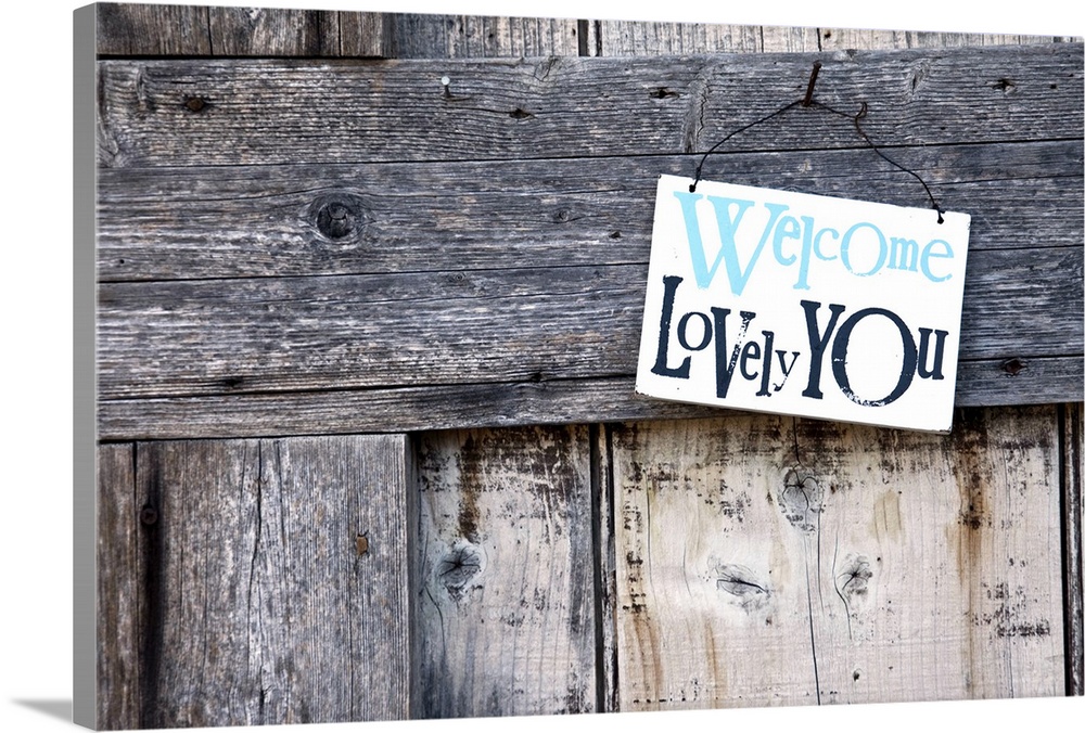 Welcome sign is hanging from nail on rustic wooden door.