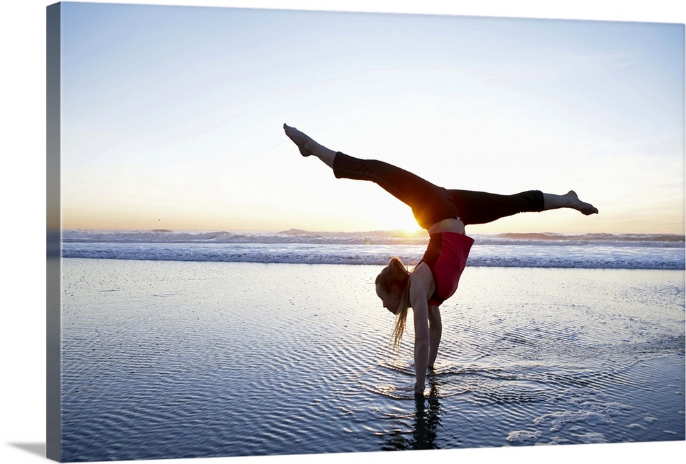 Woman doing a hand-stand on the beach at sunset.