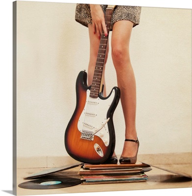 Woman holding guitar and standing on books.