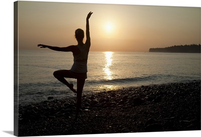 Woman practicing ballet pose on the beach, sunrise