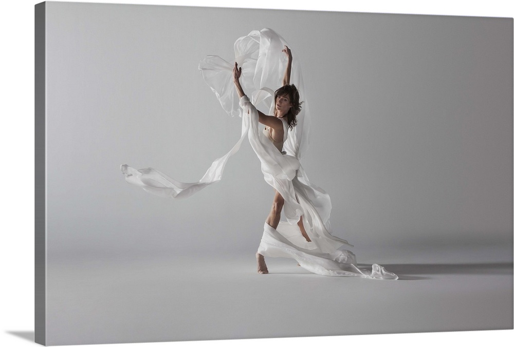 woman standing with white silk draped around her as fabric blows up and around her in wind.