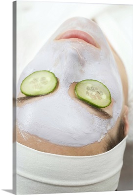 Woman with face mask and cucumber slices on eyes, close up