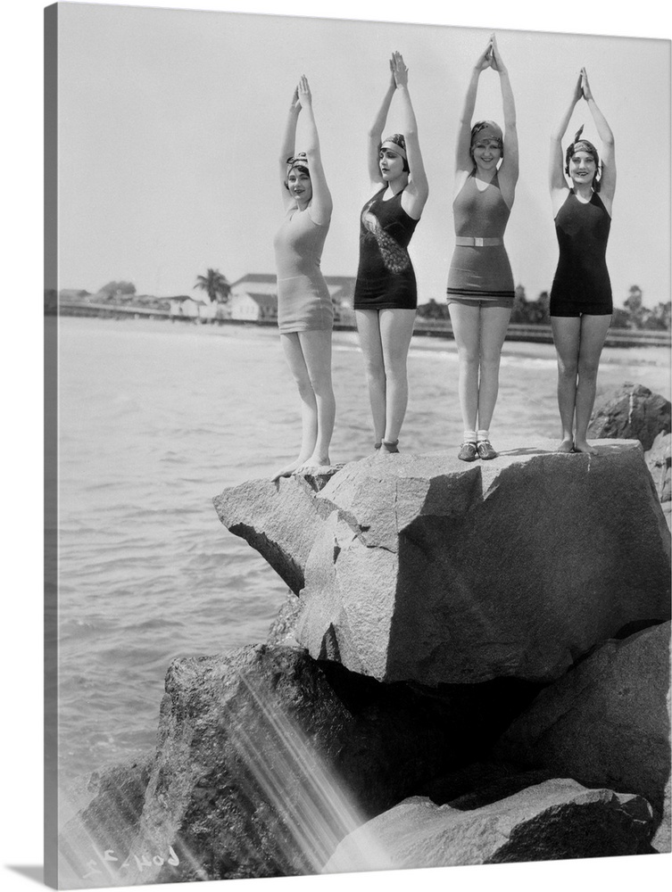 Four women wearing bathing suits are shown, posing as if ready to dive off the cliff into the water below. Dorothy Chandle...