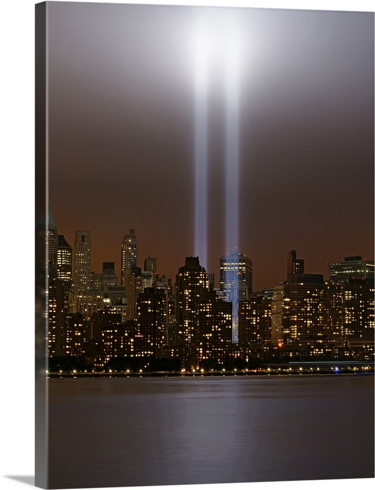 This vertical piece shows two beams of light shining up from where the twin towers stood. The skyline is lit up under a da...
