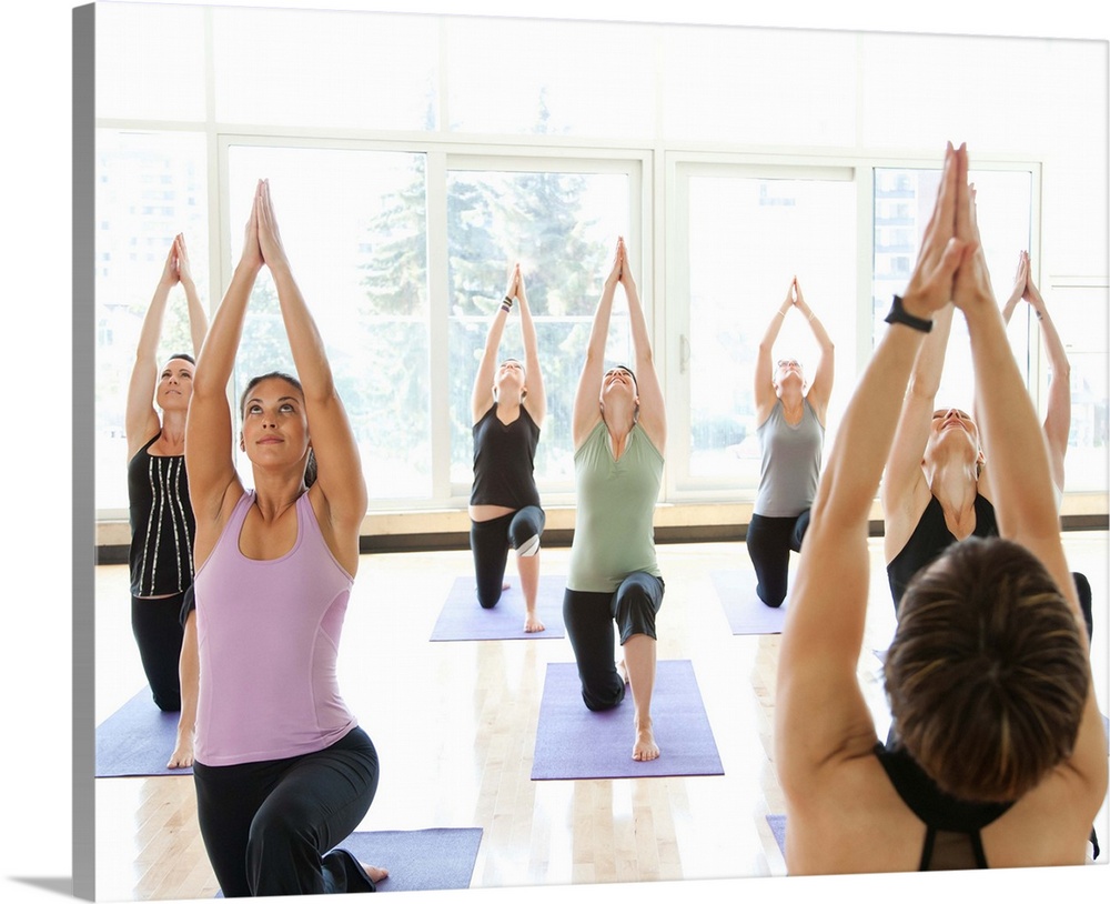 Yoga instructor leading class through the Anjaneyasana (Low Lunge Pose) in a bright, modern yoga studio