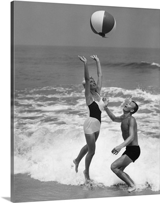 Young couple playing with beach ball at water's edge