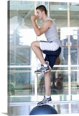 Young man doing step-up exercises on a balance ball in a fitness class
