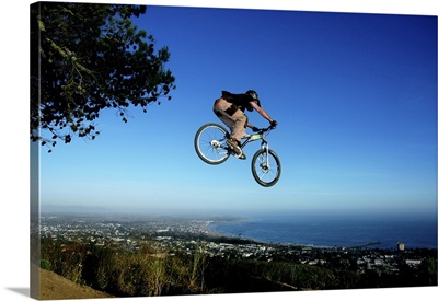 Young man goes off a jump on a mountain bike in the hills of California