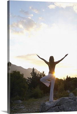Young woman balancing on rock, practicing yoga pose, rear view