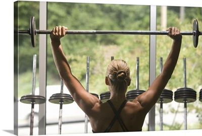 Young woman exercising with barbell, rear view