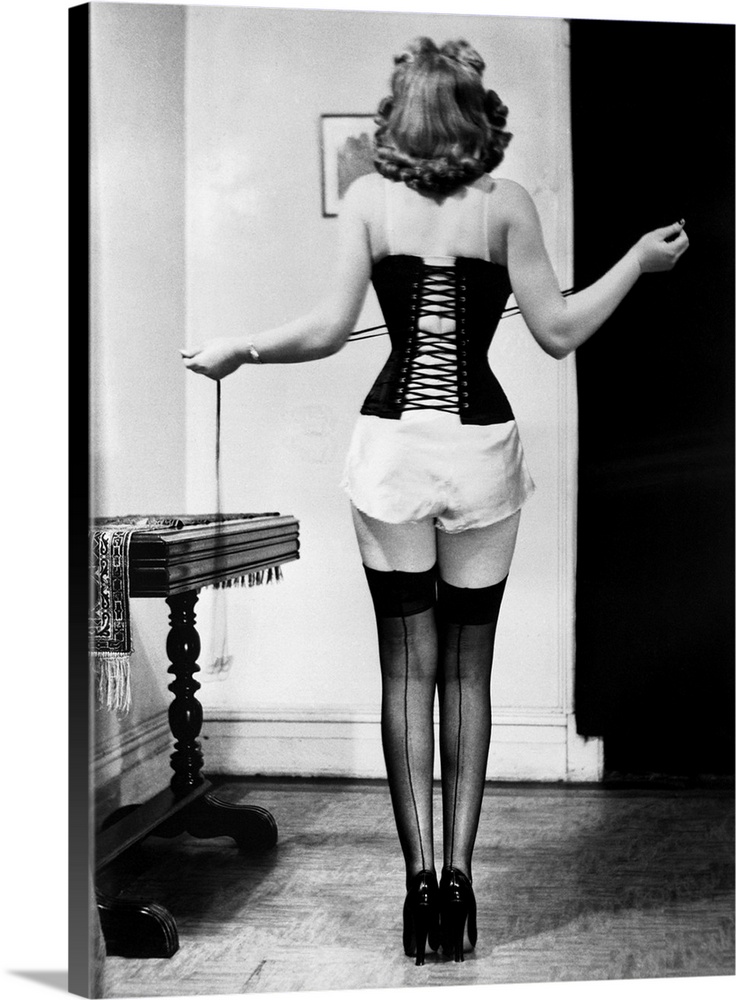 A young woman tightens the laces on her corset.
