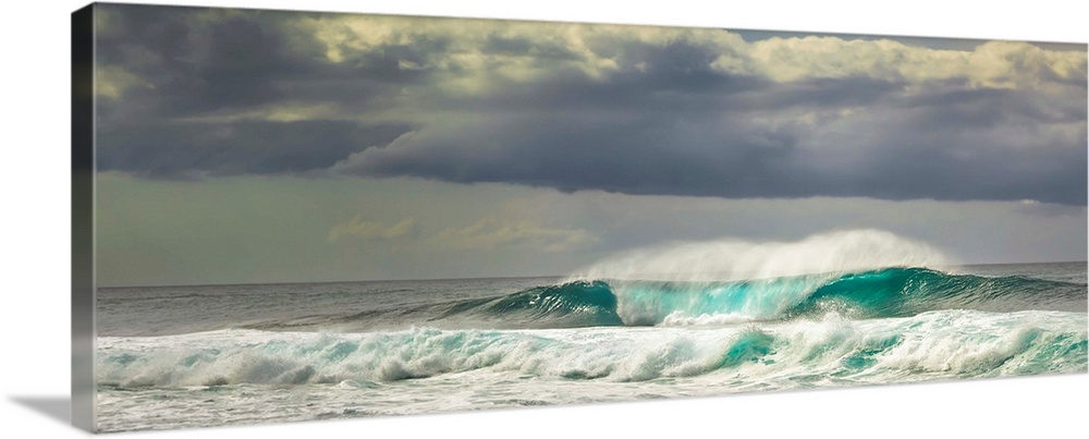Panoramic image of crashing ocean waves with large clouds above.