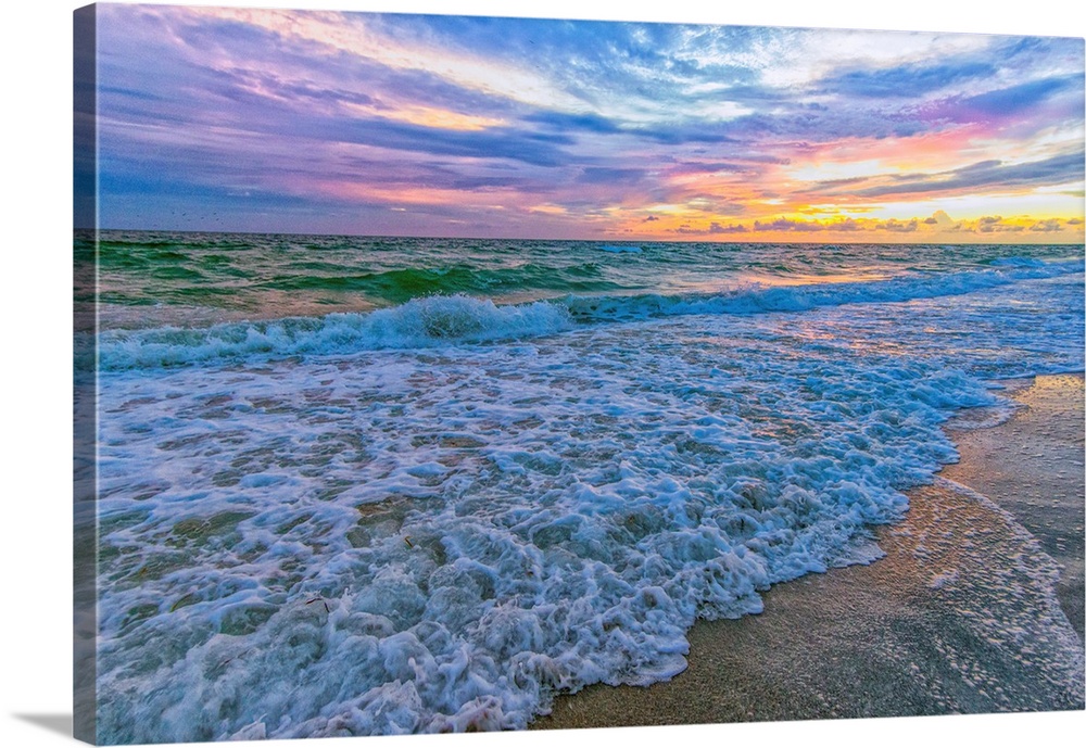 A fine art photograph of a calm sea washing up onto a sandy beach. The sunrise provides an abundance of color to the sky.